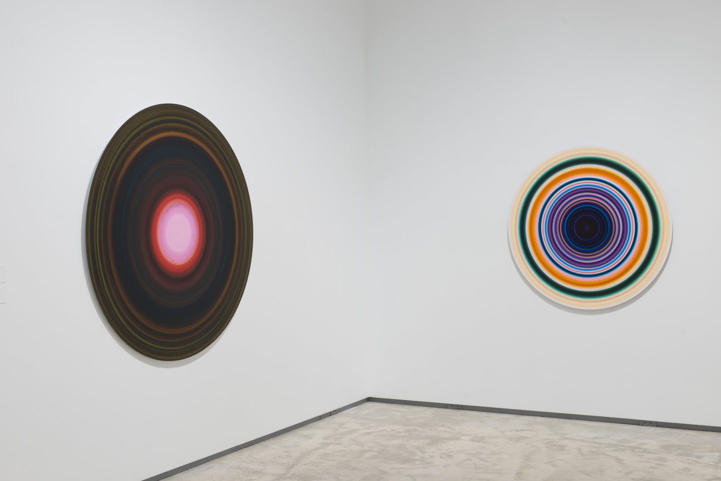 Two colourful disks, made up of concentric circles, mounted on facing walls in the corner of a white gallery