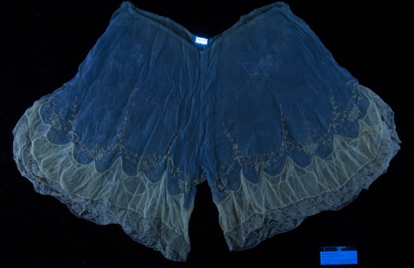 A pair of hand-embroidered underwear (likely from 1915–1925) photographed under UV light. The different ways materials fluoresce offer information about what they are made of, how they might be finished, and their condition.
