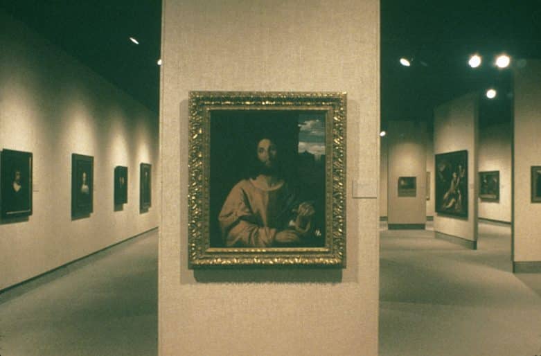 An art gallery, with walls on which paintings are mounted. Frontal view of painting of Christ in an ornamental frame.