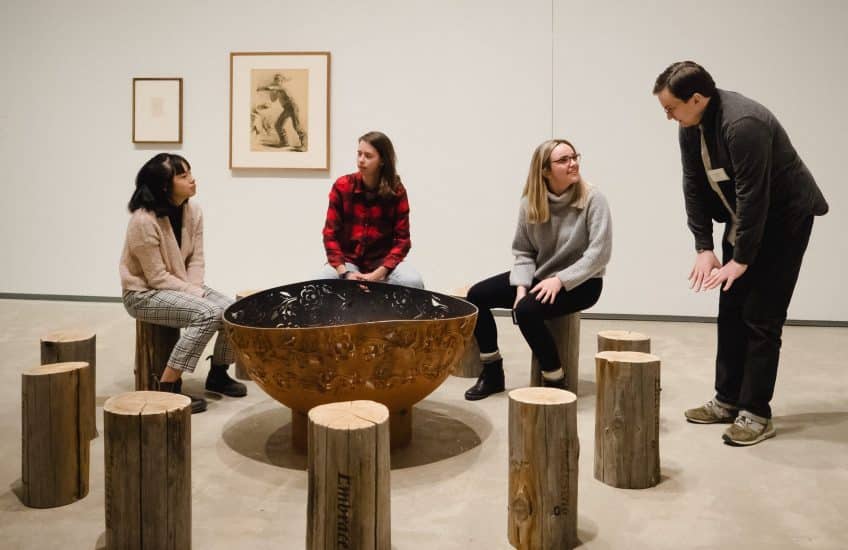 Visitors enjoy Tania Willard's "Surrounded/ Surrounding," 2018, wood burning fire ring, laser etched cedar wood logs from Secwépemc Territory from "Soundings: An Exhibition in Five Parts."