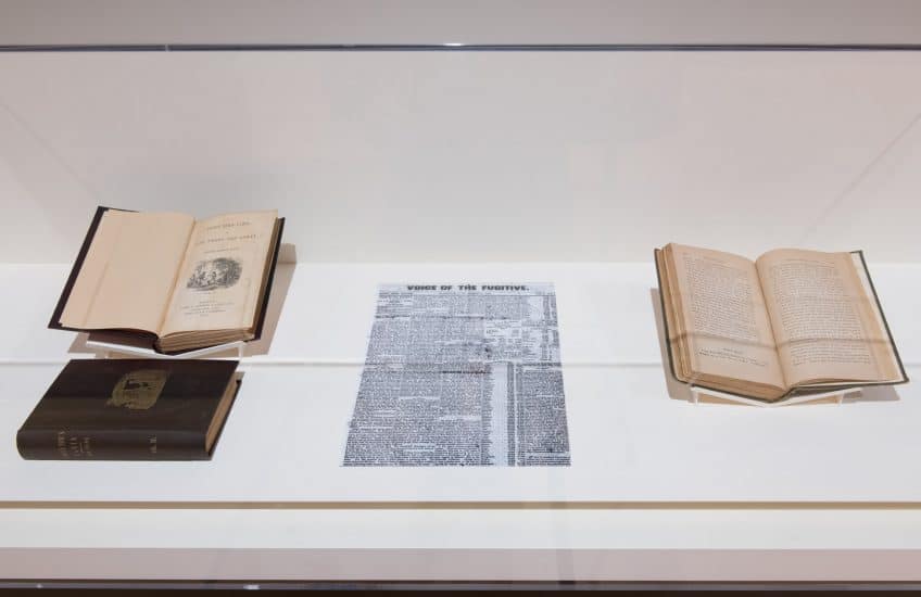 A view of books and archival reproductions installed in a case in History Is Rarely Black or White.