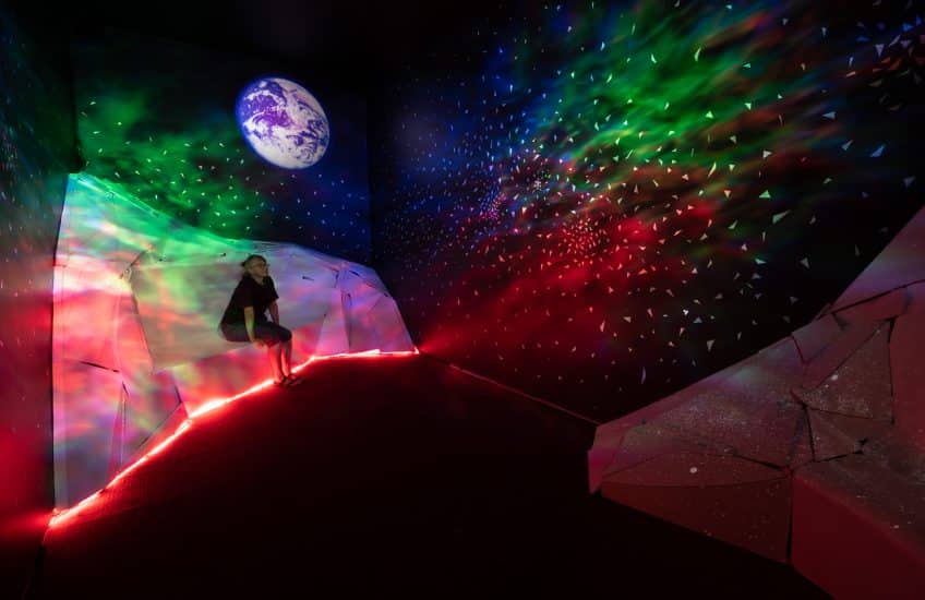Installation view of Camille Turner's "Dream Room" (2022) showing iceberg like structures to sit on with a dreamy interstellar light display in reds, greens, blues and purples.