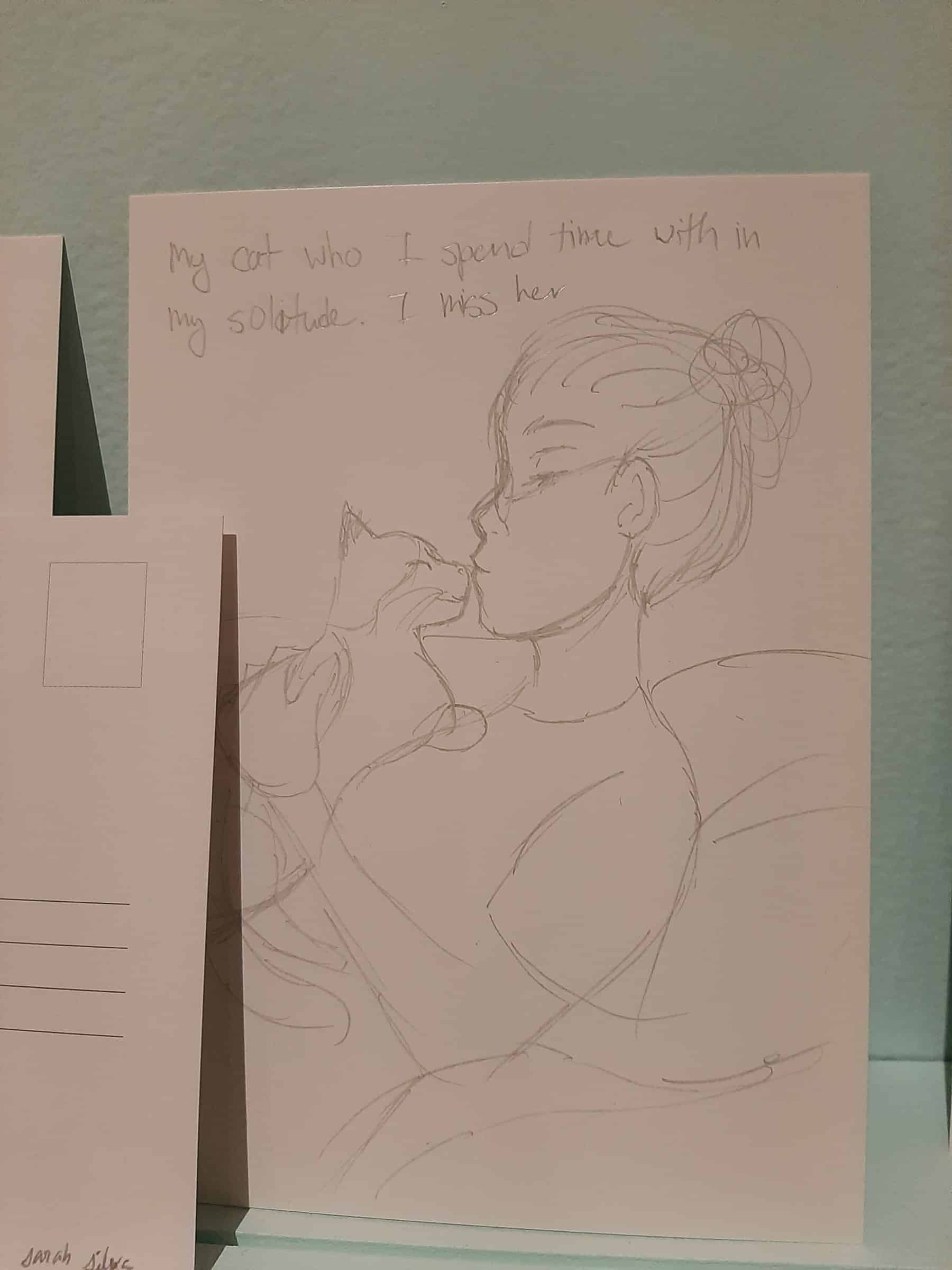 Postcard with a drawing of a girl holding a cat and text reading “My cat who I spend time with in my solitude. I miss her.”
