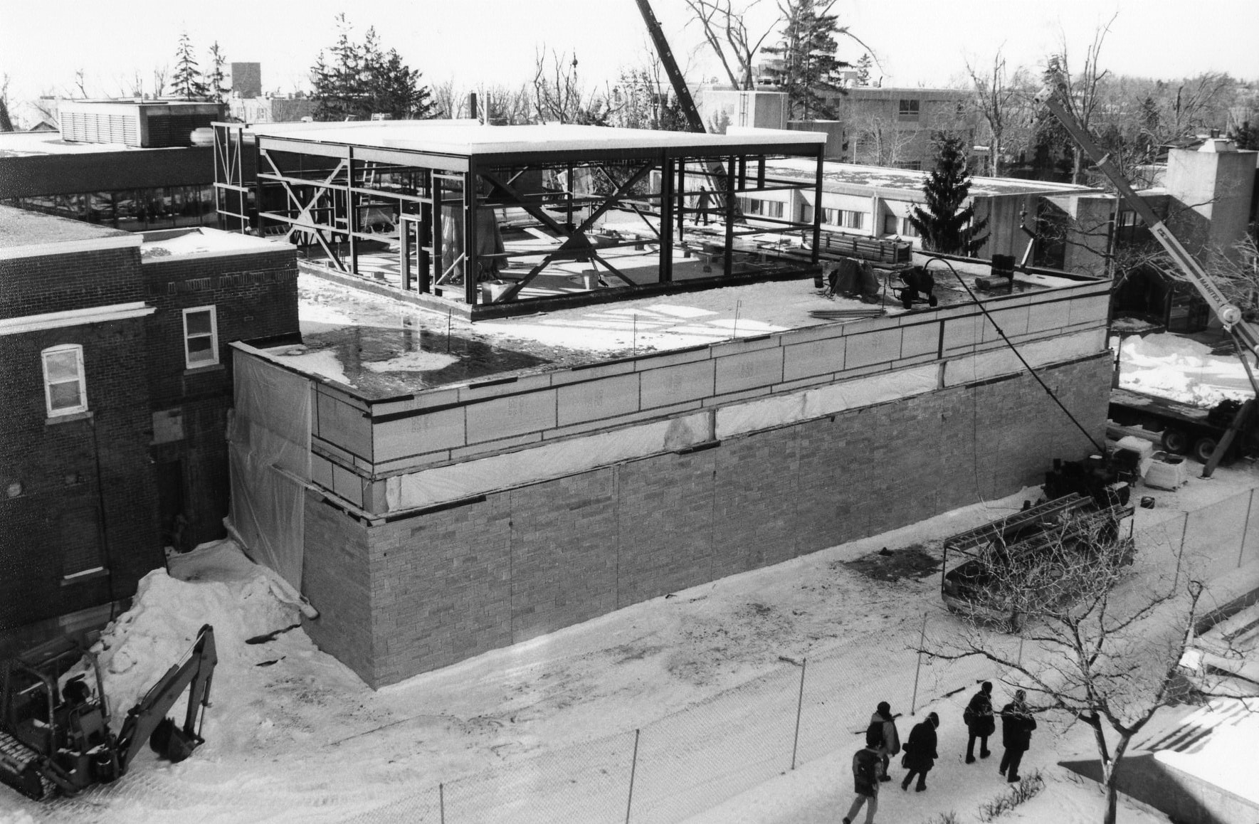 Black-and-white photograph showing a snow-covered university campus with a two-story stone building under construction.