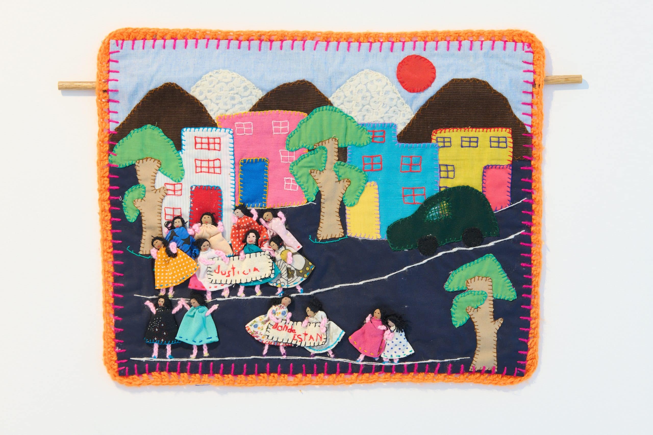 An arpillera depicting a mountainous town with colourful buildings behind people protesting.