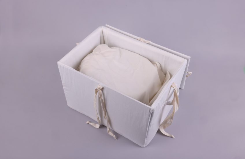 A handmade Anishinaabe box made out of naturally dyed white fabric housing a an ancestor (birch bark basket) inspired by sacred bundle teachings.