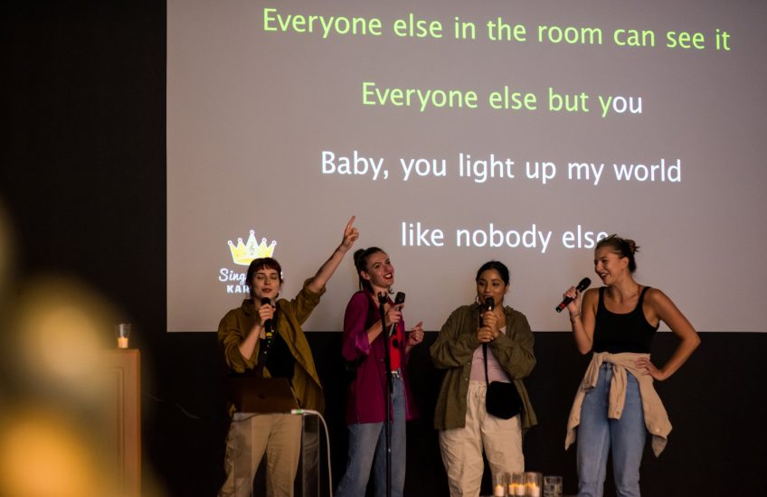 Queer Karaoke Dance Party, 2022. Four people in front of a screen singing.