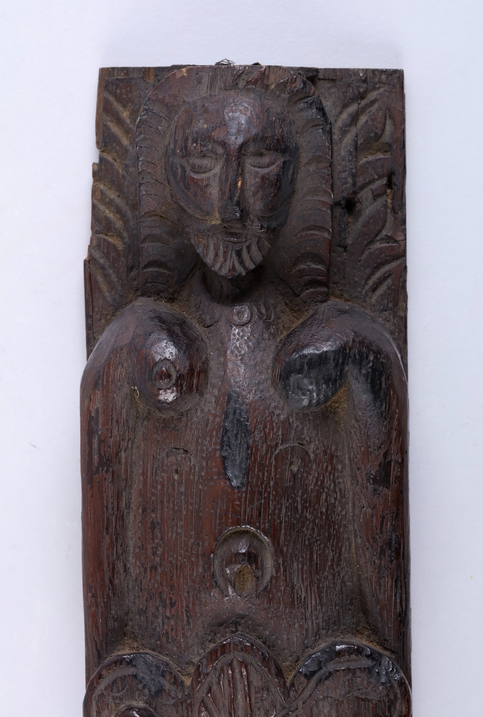 A carved wooden figure, bearded with breasts. Lower half of the body covered in leaf-like motif.