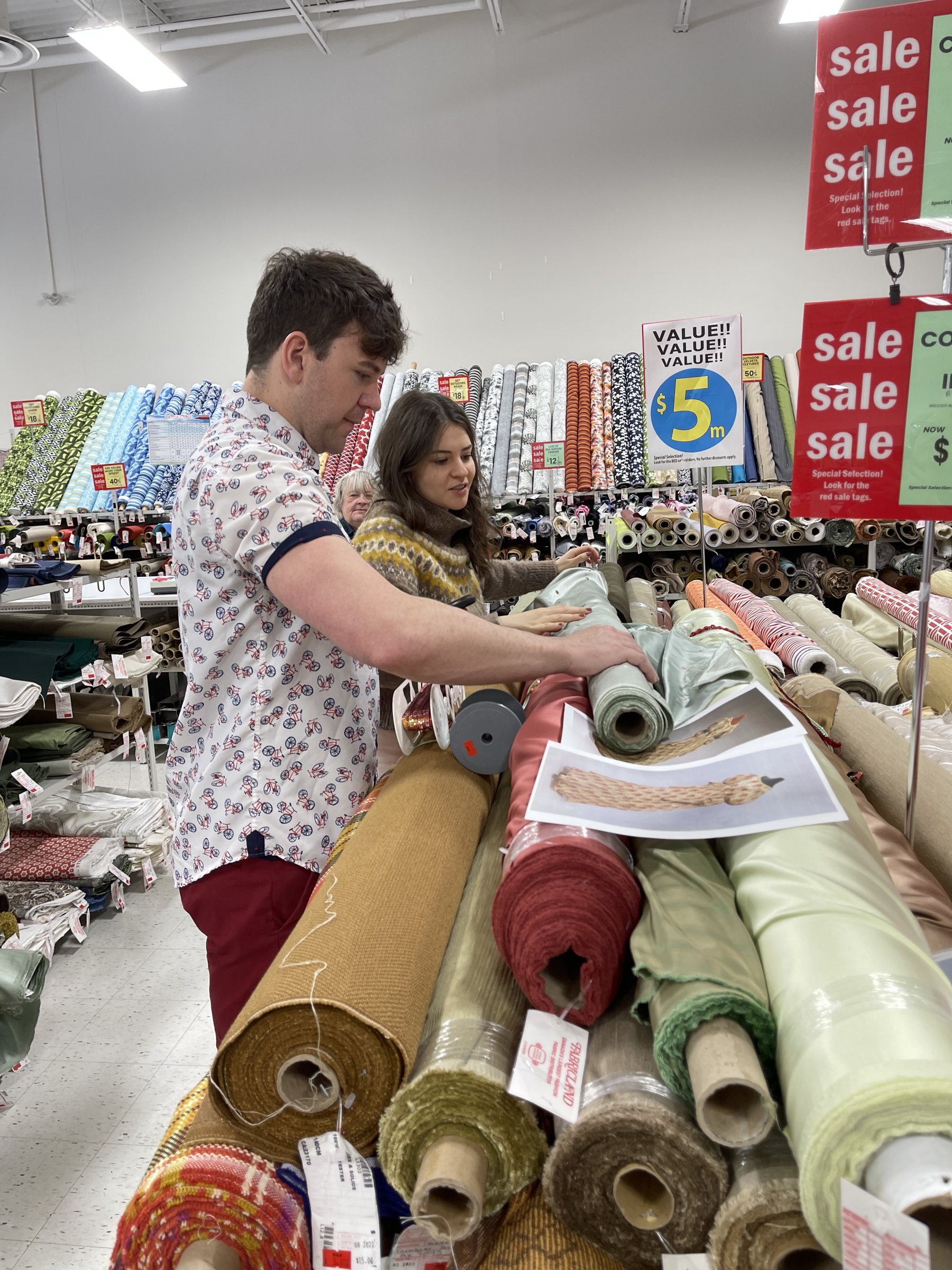 Rowena Whey and Julia Popsin-Gomes stand in front of a large selection of fabrics on rolls.