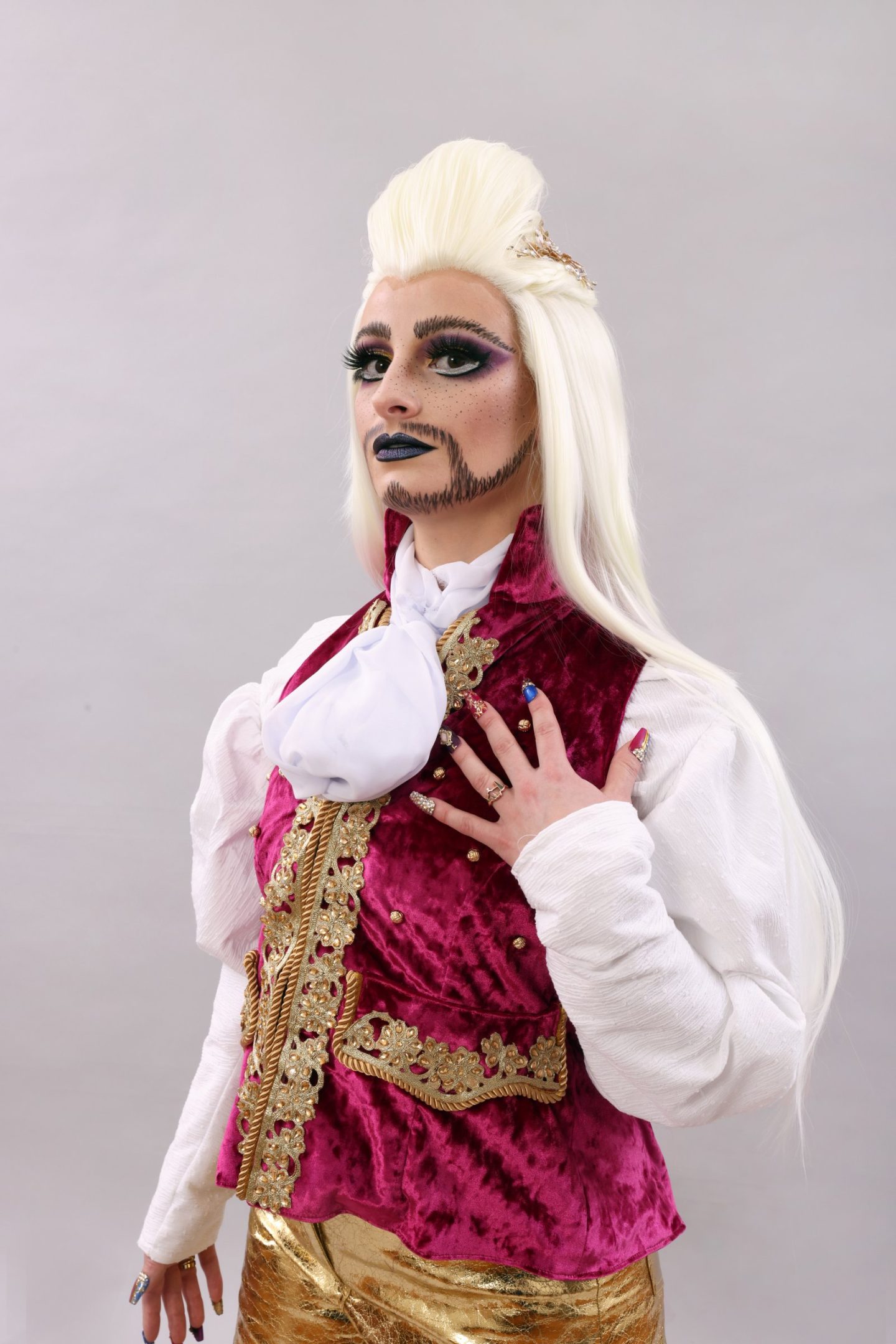 Dare De LaFemme wearing his magenta and gold embellished waistcoat, with white shirt and cravatte. He looks off camera with captivating expression.