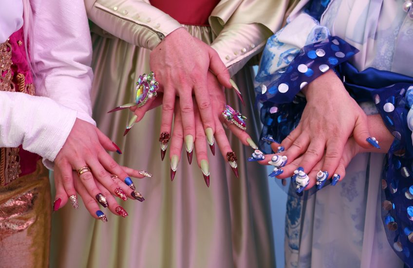 Three pairs of hands show off their extravagant, drag-inspired acrylic nails.
