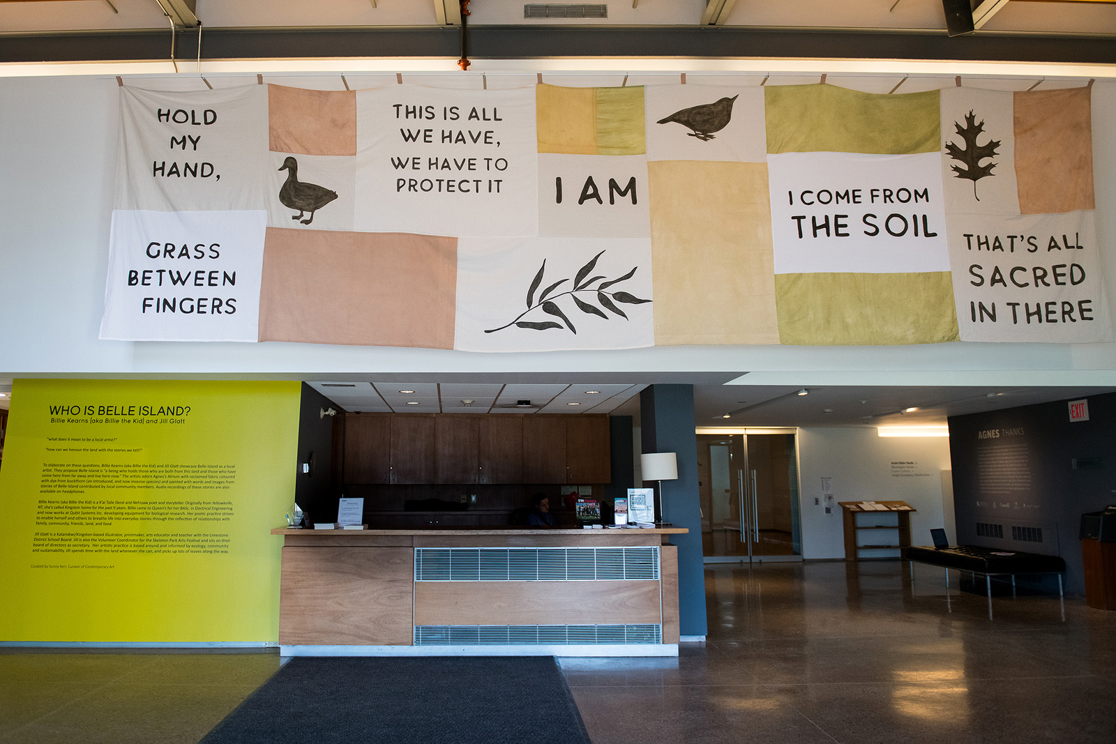 An installation view of a fabric-based artwork over a reception desk in a museum.