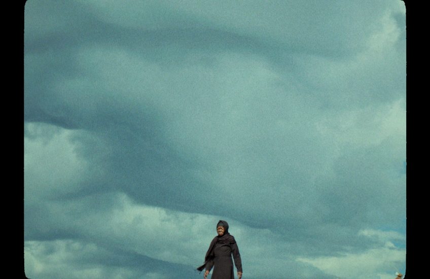 Wide angle of woman walking across landscape. Framed so the viewer can only see the clouds and sky behind her