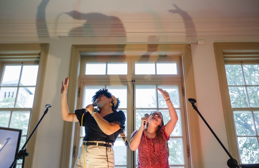 Two people with their hands stretch out above them, singing karaoke.