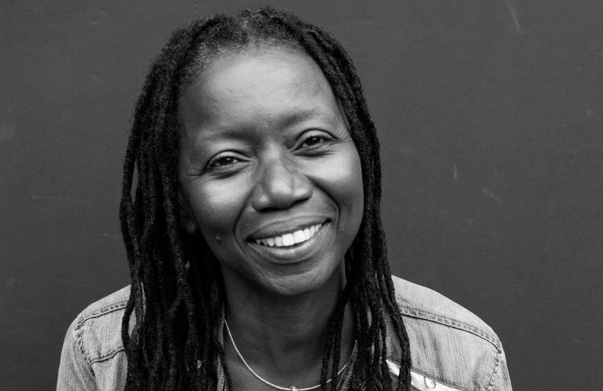 A Black woman smiles at the camera. The portrait is in black and white.