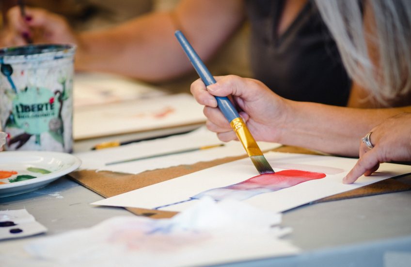 Hand holding a paintbrush as it is applied to a piece of paper