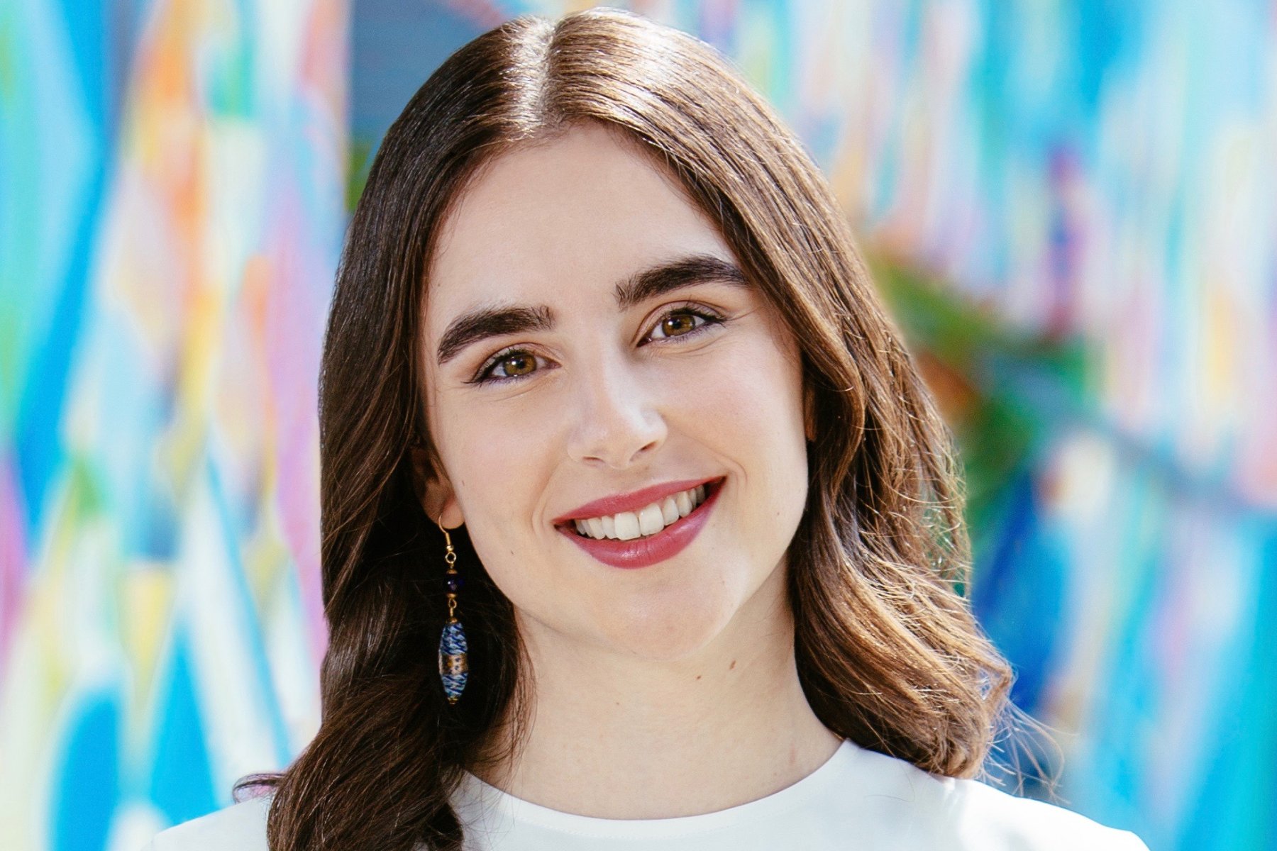 Young white woman with brown hair standing in front of a mural outside.