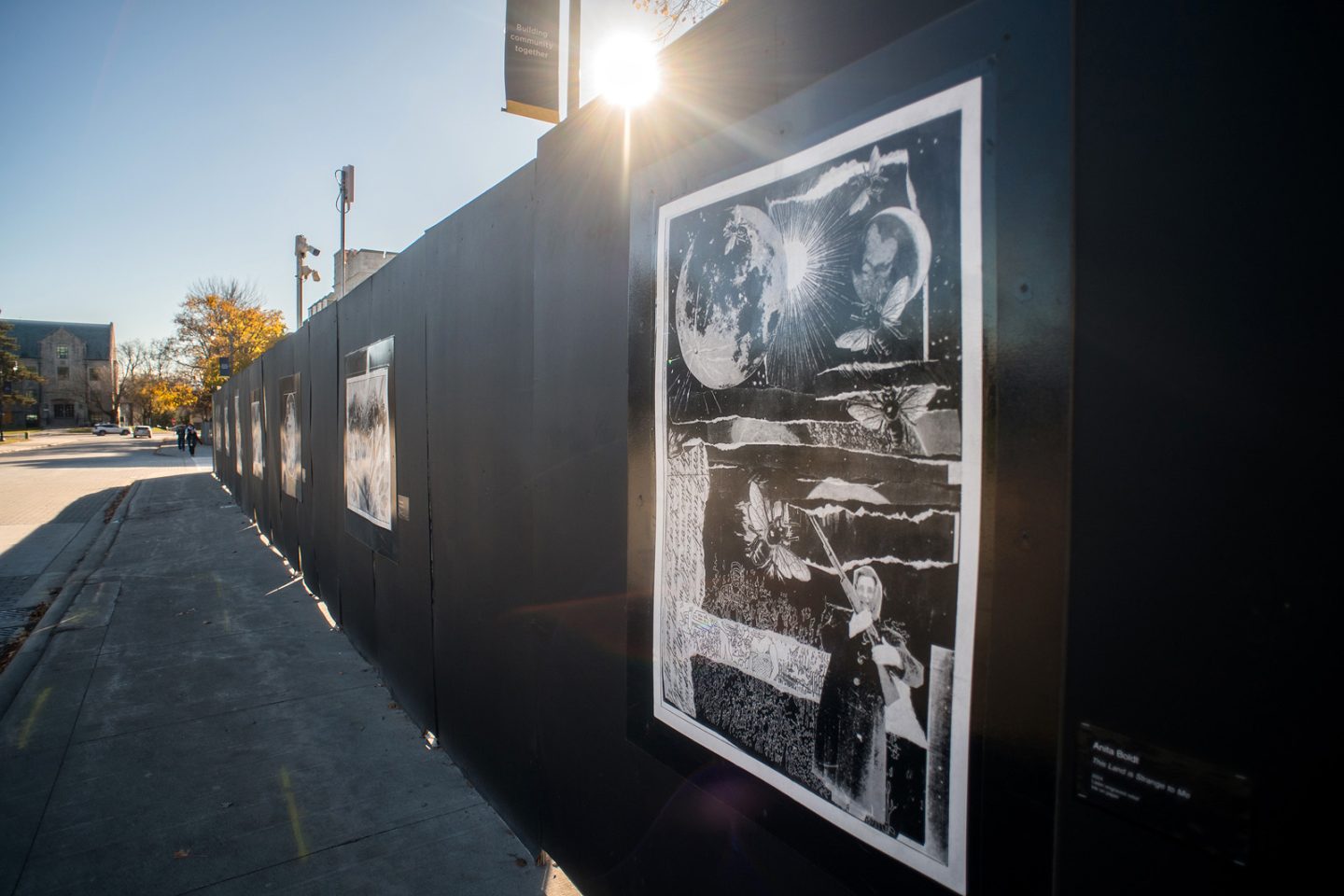 Construction Fence (hoarding) with prints pasted on them. Sidewalk and construction site visible