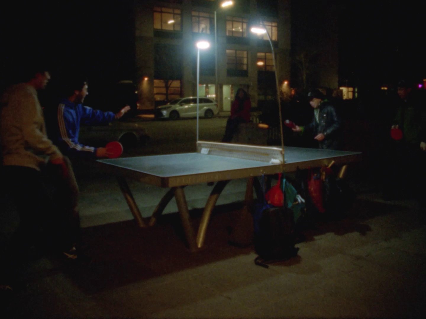 Dimly lit ping pong table outside with people playing