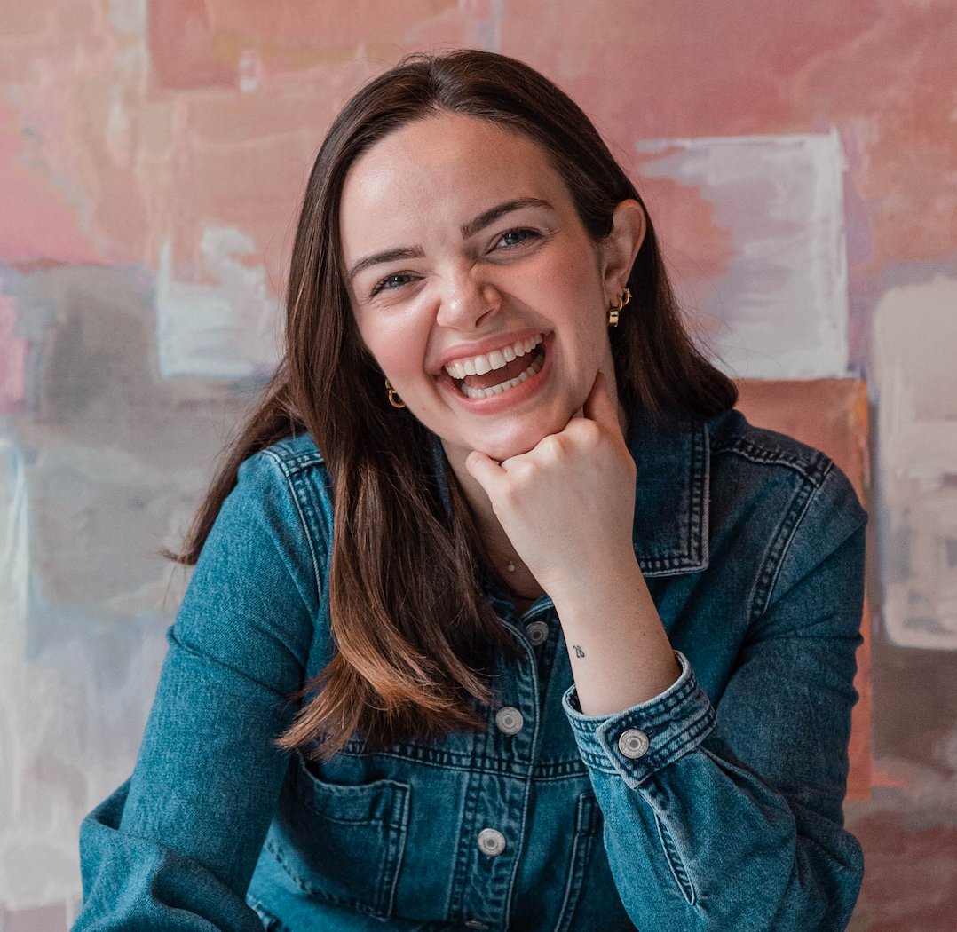 Young woman laughing while posing with her chin on her fist.