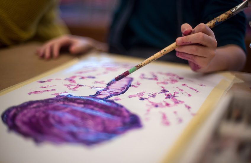 Child's hands holding a paint brush and painting a picture