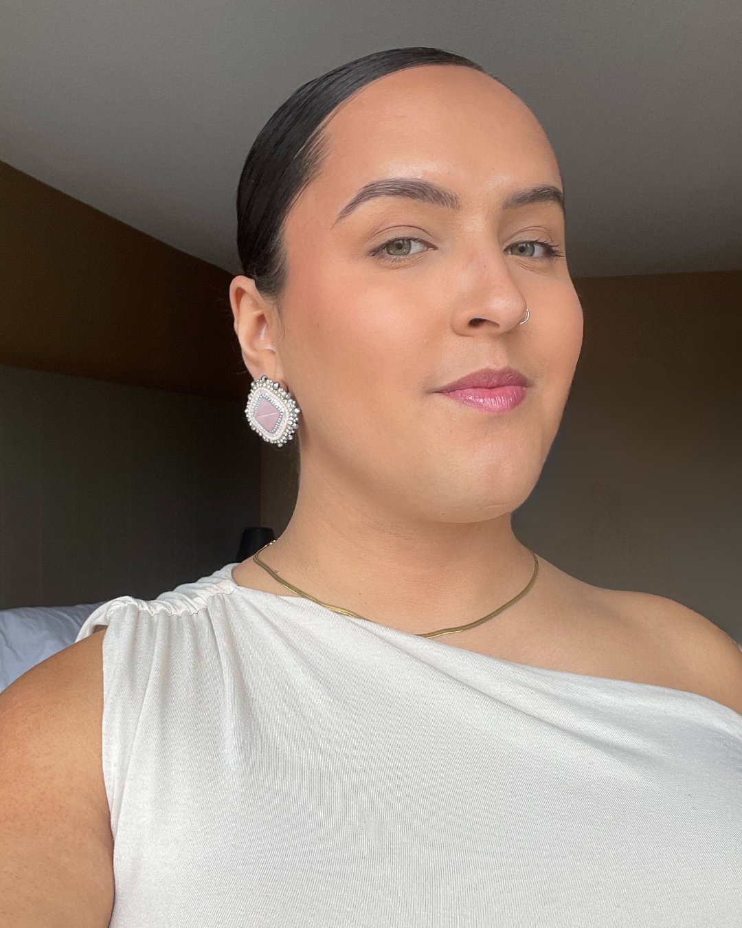 Woman looking directly at the camera. She is wearing a white one shouldered dress and white beaded earrings.