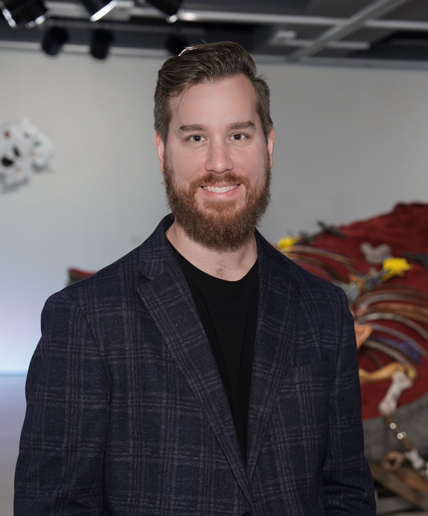 Young white man with beard looking directly at camera. He is wearing a suit jacket and tshirt