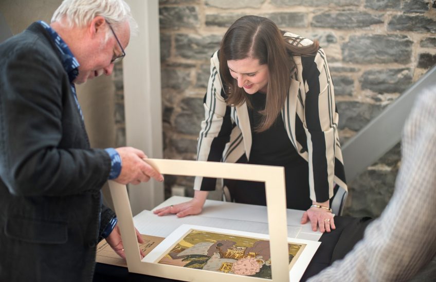 Man and woman standing over a painting, Examining it.